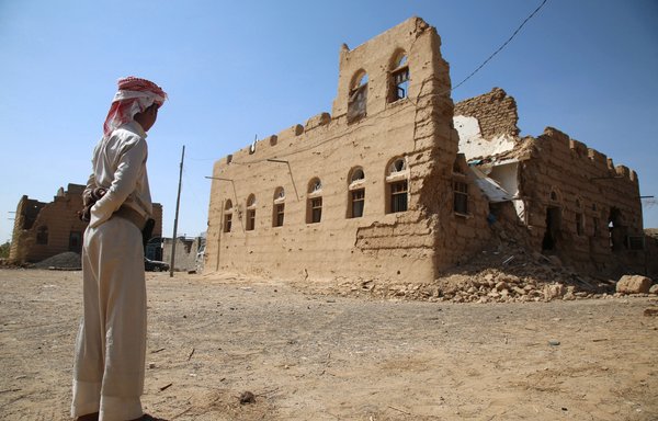 A Yemeni man stands next to a building destroyed in clashes between Yemeni forces and Houthi militants in the village of Faw on the road to Marib province, in October 2015. [Abdullah al-Qadry/AFP]