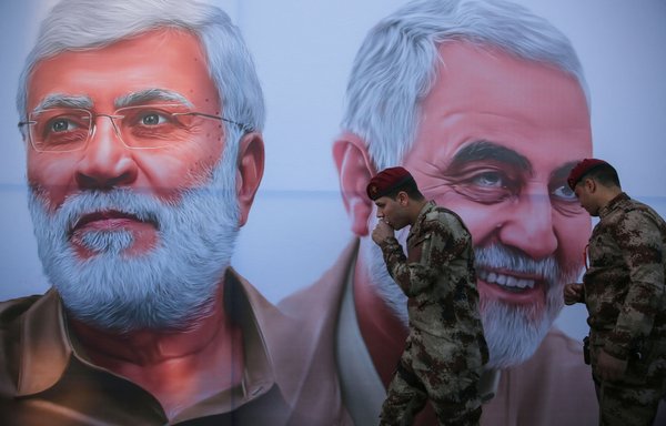 Militiamen walk past a poster depicting slain Iraqi commander Abu Mahdi al-Muhandis and IRGC Qasem Soleimani in January in Baghdad. [AHMAD AL-RUBAYE / AFP]