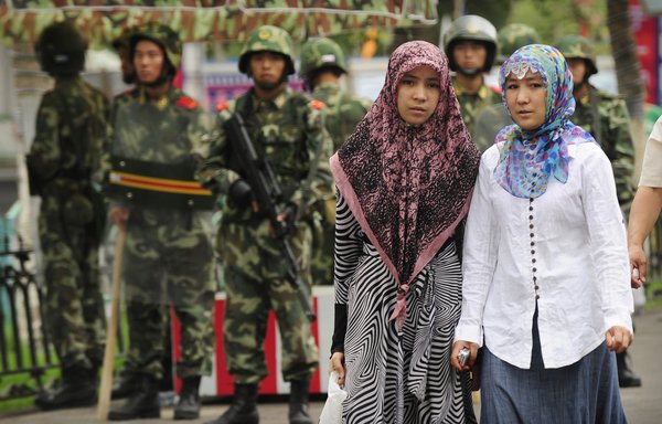 Two Muslim women pass Chinese paramilitary policemen standing guard outside the Grand Bazaar in Urumqi, Xinjiang. Muslim women in Chinese 're-education' camps in the Xinjiang region are systematically raped, tortured and sexually abused, former detainees and a guard recently revealed. [Peter Parks / AFP]