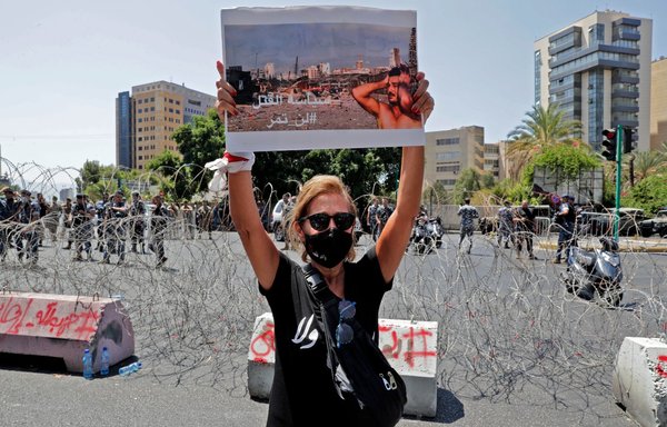 A woman holds a sign showing a photo of a man reacting at the scene of the 2020 Beirut port blast, at a protest near the UNESCO palace in the Lebanese capital on August 12, ahead of a parliamentary meeting on the blast investigation. [Anwar Amro/AFP]