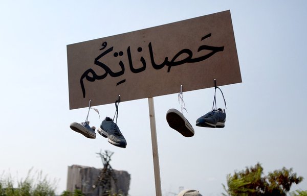 متظاهر يرفع لافتة كتب عليها ʼحصاناتكمʻ وعلقت عليها أحذية، خلال تظاهرة في مرفأ العاصمة اللبنانية بيروت في 4 آب/أغسطس بالذكرى الأولى للانفجار الذي دمر المرفأ والمدينة. [باتريك باز/وكالة الصحافة الفرنسية]