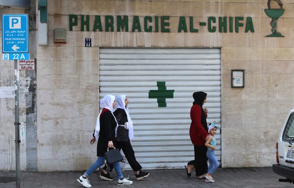 People walk in front of the shuttered door of a pharmacy in Beirut, during a nationwide strike of pharmacies to protest against a severe shortage of medicine, on July 9. [Anwar Amro/AFP]