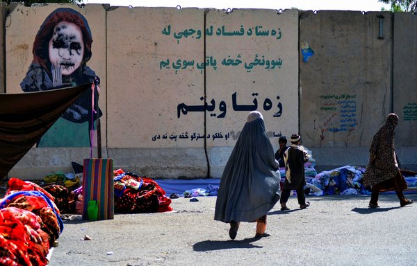 Covered women walk past a vendor selling secondhand clothes near a defaced mural at a market in Kandahar on September 22. [Javed Tanveer/AFP]