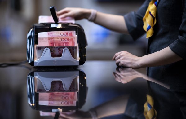 A bank employee uses a money counting machine to count out 100 yuan notes at a bank in Shanghai, China. [Johannes EISELE / AFP]