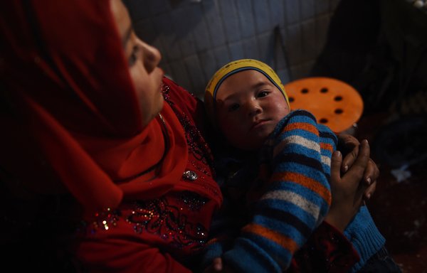 A Muslim woman holds her baby at a market in Hotan, in China's western Xinjiang region. Former detainees and guards revealed that Muslim women in Beijing-run camps in the region are systematically raped, tortured and sexually abused. [Greg Baker/AFP]