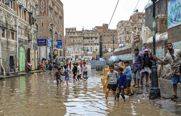 Children walk through a flooded street following heavy rainfall in the old city of Yemen's capital Sanaa on August 3. [Mohammed Huwais/AFP]