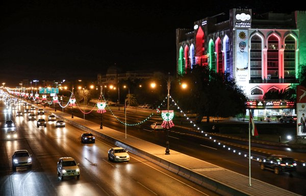 Vehicles drive along a main road past a building of the Oman Arab Bank, lit up with the national colours on the occasion of the Omani national day, on November 16, 2020. [Mohammed Mahjoub/AFP]