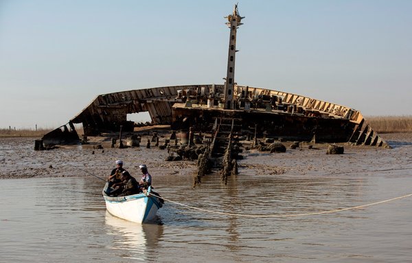 Iraqi men fish in their boat anchored in the Shatt al-Arab waterway next to the wreckage of a ship which was sunk during the 1980s Iraq-Iran war, in the southern Iraqi port city of al-Faw on October 26. [Hussein Faleh/AFP]