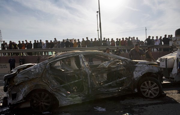 A picture shows bystanders near a destroyed car in the southern Iraqi city of Basra after at least four civilians were killed and four more wounded in a motorcycle bombing near a hospital on December 7. [Hussein Faleh/AFP]