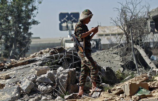A Houthi fighter looks at his phone while standing amid the rubble of a building destroyed following an Arab coalition air strike targeting Sanaa International Airport on December 21. The retaliatory strike followed a drone attack on Saudi Arabia's Abha airport. [Mohammed Huwais/AFP]