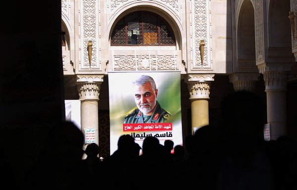 People stand beneath a portrait of the late IRGC Quds Force commander Qassem Soleimani during a vigil in Sanaa on January 2, 2021, ahead of the first anniversary of his death. [Mohammed Huwais/AFP]