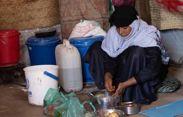 A woman prepares food at a displacement camp in Yemen. Most Yemeni families have been forced to reduce the number of daily meals due to increasing prices and inflation. [Norwegian Refugee Council]