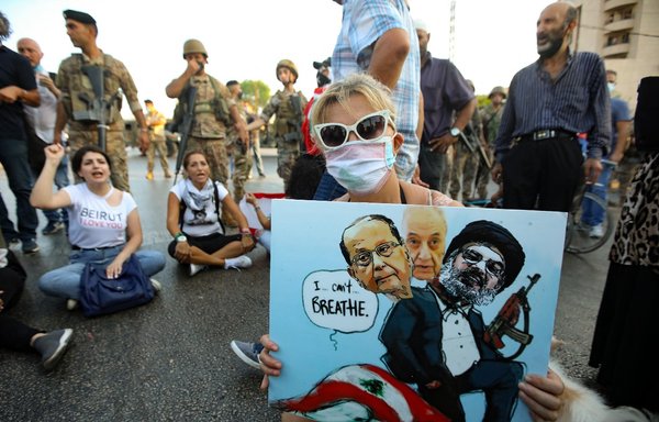 A protester in Baabda holds a cartoon of President Michel Aoun, Parliament Speaker Nabih Berri and Hizbullah chief Hassan Nasrallah sitting atop a national flag during a September 12, 2020 demonstration against the lack of progress in the Beirut port explosion probe. [Anwar Amro/AFP]