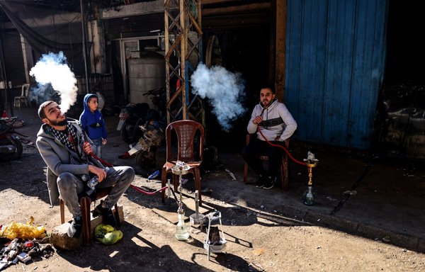 Lebanese men smoke waterpipes as they take a break outside their workshop in an alley of the northern city of Tripoli's impoverished neighbourhood of Bab al-Tabbaneh, on January 17. [Joseph Eid/AFP]