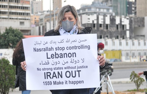 متظاهر يحمل في بيروت يوم 4 آذار/مارس لافتة تندد بأخذ حزب الله وإيران لبنان رهينة له وتطالب بتنفيذ قرار مجلس الأمن رقم 1559 بشكل كامل. [زياد حاتم/المشارق]