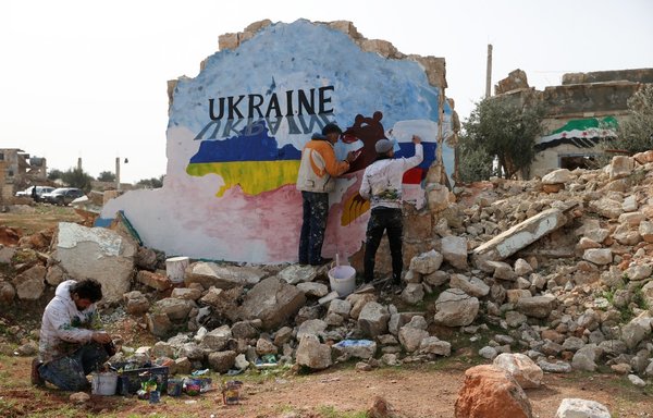 Syrian artists paint a mural to protest against Russia's military operation in Ukraine amid the destruction in the opposition-held town of Binnish in Syria's Idlib province on February 24. [Omar Haj Kadour/AFP]