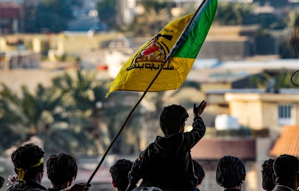 Young men raise the flag of Kataib Hizbullah during commemorations marking the second anniversary of the killing of top Iranian commander Qassem Soleimani and Iraqi commander Abu Mahdi al-Muhandis, in the southern Iraqi city of Basra, on January 8. [Hussein Faleh/AFP]