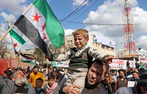 پسری سوری که صورتش با رنگ‌های پرچم اوکراین رنگ‌آمیزی شده است ٢٤ اسفند در راهپیمایی برگزار شده در استان ادلب به مناسبت یازدهمین سالگرد قیام علیه رژیم این کشور شرکت می‌کند. [عمر حاج خدور/خبرگزاری فرانسه]