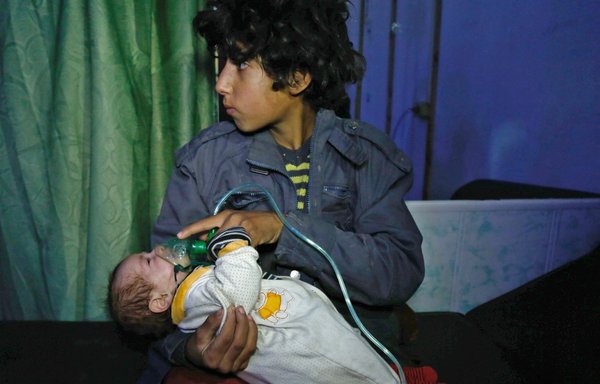 A Syrian boy holds an oxygen mask over the face of an infant at a makeshift hospital following a reported gas attack blamed on the regime on the opposition-held besieged town of Douma on the outskirts of Damascus on January 22, 2018. [Hasan Mohamed/AFP]