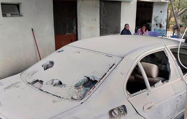 People react next to a damaged vehicle near the site of an explosion at a building that belonged to the Islamic Risala Scouting Association, affiliated with the Amal movement, in Bnaafoul, near Sidon, on April 12. [Mahmoud Zayyat/AFP]