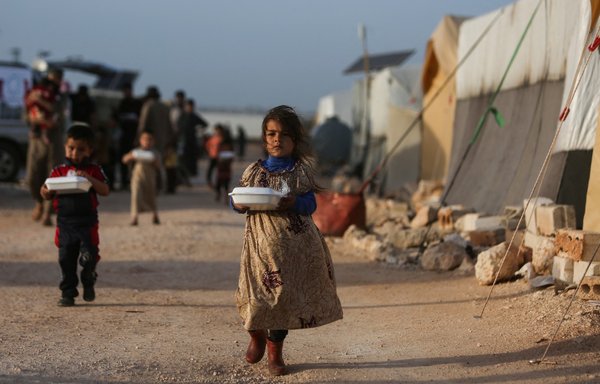 Displaced Syrian children return to their tents with boxes of food distributed by a local charity during Ramadan, at a camp for displaced people on the outskirts of the town of Dana, in Idlib province, on April 3. [Aaref Watad/AFP]
