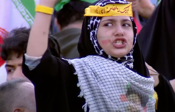 فتاة ترتدي عصابة رأس مكتوب عليها 'أنا استجيب لدعوتك يا خامنئي' تشارك في احتفال غنائي في مجمع أزادي الرياضي بطهران في أواخر شهر أيار/مايو بعد إصدار أغنية جديدة مؤيدة لخامنئي بعنوان "تحية أيها القائد!". [لقطة شاشة من IRIB]