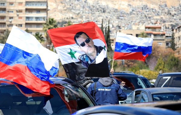 سوريون يرفعون العلم الروسي مع صورة للرئيس بشار الأسد خلال تجمع لدعم روسيا في دمشق بتاريخ 25 آذار/مارس. [لؤي بشارة/وكالة الصحافة الفرنسية]