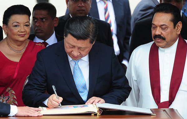 Chinese President Xi Jinping (centre) signs a visitor's book as then-Sri Lankan President Mahinda Rajapaksa (right) looks on during a welcome ceremony at the Bandaranaike International Airport in Katunayake on September 16, 2014. [Lakruwan Wanniarachchi/AFP]
