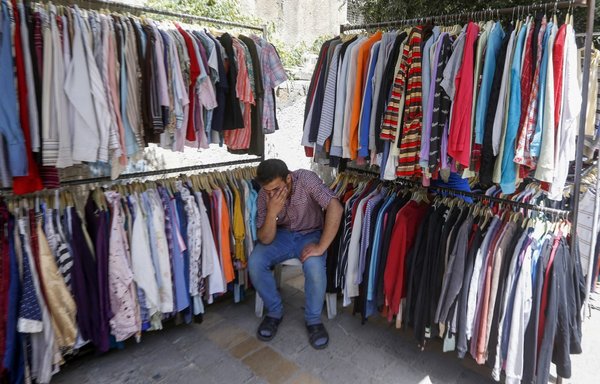 A Syrian man waits for customers at a secondhand clothing shop at a market in Damascus on May 17, 2020, amid a severe and ongoing economic crisis. [Louai Beshara/AFP]