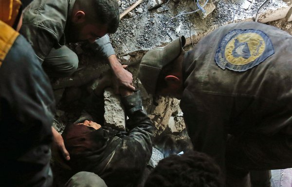 Members of the White Helmets rescue a woman from the rubble of a building after an air strike in Douma, Eastern Ghouta, on March 19, 2018. [Hasan Mohamed/AFP]