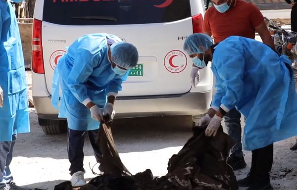 Members of the Kurdish Red Crescent and the Manbij health committee catalogue the remains of ISIS victims found in a mass grave in the city, along with their personal belongings, in a screenshot from a video posted online on July 27. [Manbij TV Facebook page]