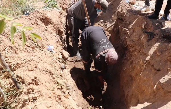 Municipal workers in Manbij, seen here in a screenshot from a video posted on July 27, exhume the bodies of ISIS victims from a mass grave they discovered while doing excavation work to upgrade the sewage system. [Manbij TV Facebook page]