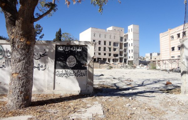 A photo taken September 25, 2016, shows the ISIS flag painted on the wall outside the Manbij hotel in Manbij, which ISIS used as a prison. A mass grave containing the remains of the group's civilian victims has been found near the site. [Ayham al-Mohammad/AFP]