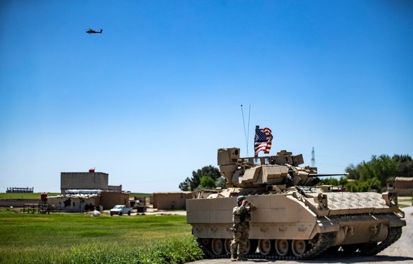 In this file photo a US Apache attack helicopter flies over Bradley Fighting Vehicles on patrol in the countryside of the Kurdish-majority city of Qamishli, al-Hasakeh province, Syria, April 20. US President Joe Biden on August 23 ordered air strikes in eastern Syria targeting facilities used by Iranian-backed militias, a US military spokesman said. [Delil Souleiman/AFP]