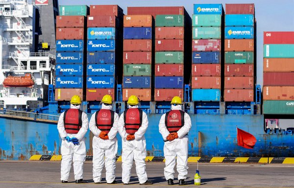 Employees wearing personal protective equipment stand by a cargo ship at a port in Qingdao, China, on January 14. [STR/AFP]