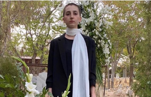 A young woman whose mother was killed in Iran's September protests stands over her mother's grave, holding her hair, which she has cut off. Her mother's picture is placed on the makeshift gravestone. [Social media]