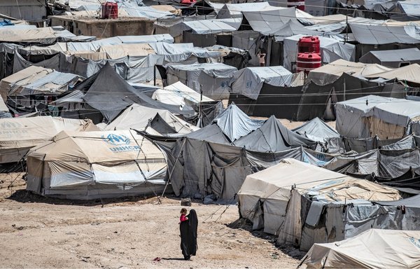 A woman walks carrying a child at al-Hol camp, which holds relatives of suspected ISIS fighters, in Syria's northeastern al-Hasakeh province on August 18, 2021. [Delil Souleiman/AFP]