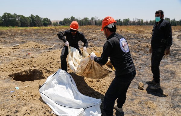 Members of the local forensic medicine team inspect human remains found by the al-Raqa Civil Council's first responders at a mass grave site in the Fukheikha agricultural suburb about 10km away from al-Raqa, on July 4, 2019. [Muhammad Ahmad/AFP]