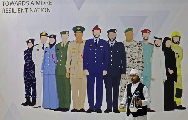 A coffee steward walks past a poster depicting Abu Dhabi police uniforms during the opening of the International Exhibition for National Security and Resilience in the Emirati capital, on October 10. [Karim Sahib/AFP]