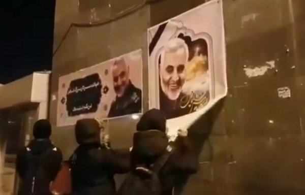 Iranian youth tear a poster of the late IRGC Quds Force commander Qassem Soleimani off a wall on a street in Iran. [Photo circulated on social media]