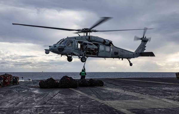 Sailors assigned to the Nimitz-class aircraft carrier USS George H.W. Bush attach a cargo hook to an MH-60S Nighthawk helicopter, during a replenishment at sea on December 11. [US Navy]