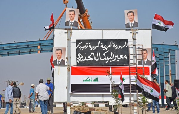 صور للرئيس السوري بشار الأسد والعلمين السوري والعراقي تظهر على المعبر الحدودي بين القائم في العراق وألبو كمال في سوريا من الجانب العراقي للحدود بتاريخ 30 أيلول/سبتمبر 2019. [معاذ الدليمي]
