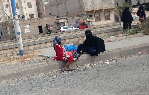 Umm Malak and her daughter, displaced to Sanaa from al-Hodeidah, beg beside the road. [Haitham Mohammed/Al-Mashareq]