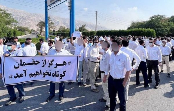 Striking Iranian oil and gas workers hold a banner that reads: We will #never give up our rights. [Iran International]