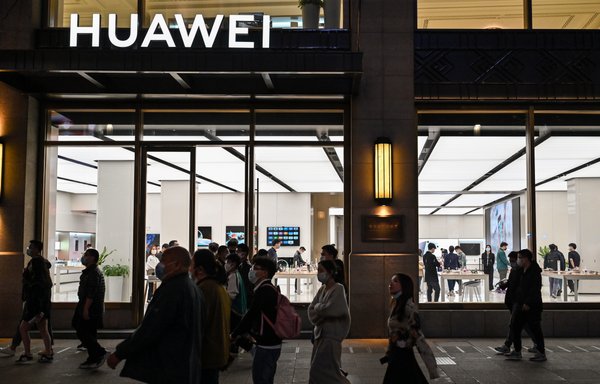 People walk next to a Huawei shop along a pedestrian street surrounded by shops and shopping malls in Shanghai last October 12. [Hector Retamal/AFP]
