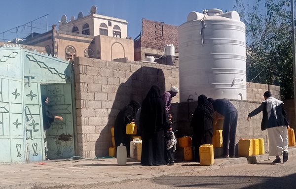 زنان و کودکان برای تأمین نیاز آب یک روزشان، ظرف‌های آب خود را در محل‌های توزیع عمومی پر می‌کنند. [هیثم محمد/المشارق]