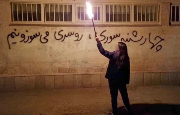 A girl celebrates the traditional fire festival on a street in Iran on March 14 without a headscarf. She is standing in front of a slogan that reads, 'We will burn our scarves on Wednesday eve.' [Twitter]