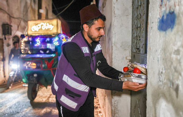 A volunteer from the charity Violet Organisation hands out food packages for the suhur meal consumed before the next day's fast during the Muslim holy month of Ramadan in the old city of Syria's northwestern city of Idlib early on April 19. [Omar Haj Kadour/AFP]