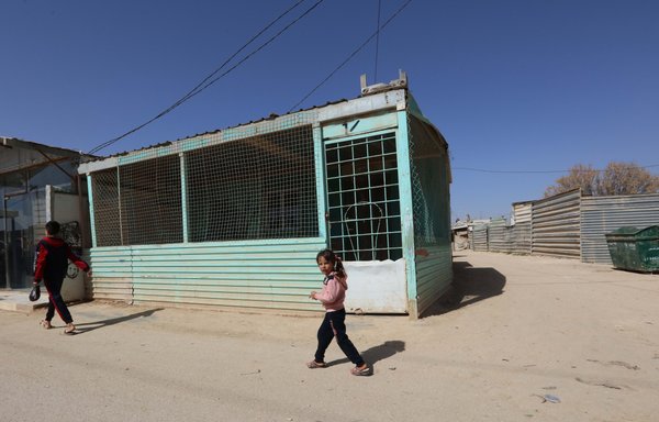 أطفال لاجئون سوريون يمشون أمام مبنى مؤقت في مخيم الزعتري للاجئين يوم 13 آذار/مارس. [محمد أبو غوش]