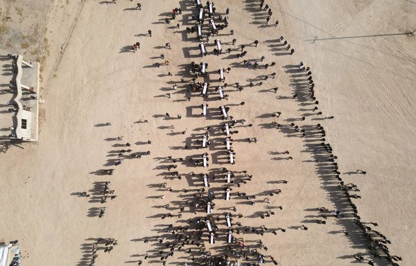 An aerial picture shows mourners carrying coffins during a mass funeral for Yazidi victims of ISIS whose remains were found in a mass grave, in the Sinjar district of Kojo on December 9, 2021. [Zaid al-Obeidi/AFP]